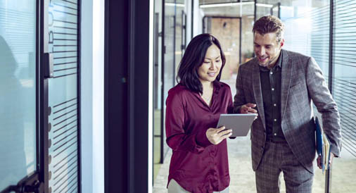 Two people in office hallway looking at tablet computer